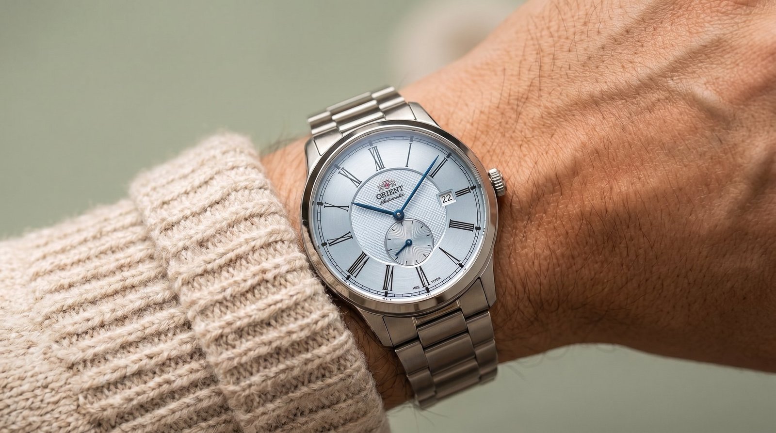 Relógio Orient Special Calibers no pulso, com pulseira de aço e suéter de tricô cru
